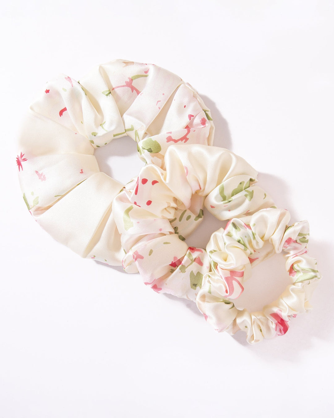 Two floral patterned fabric scrunchies in white and pastel colors from the Lovely Flowers Silk Scrunchies Set 3-Pack by SusanSilk, crafted from luxurious silk, are placed on a white background.