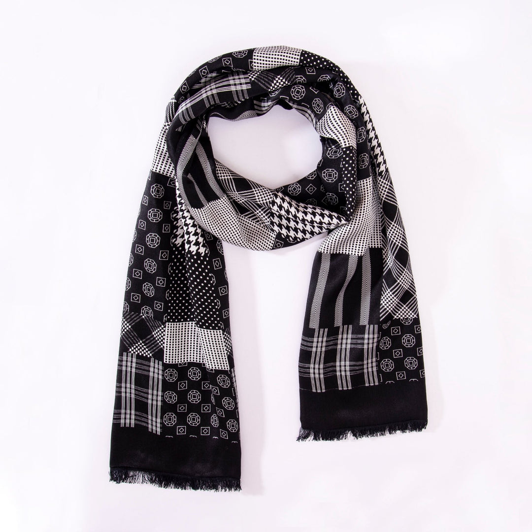 The Mix Pattern Long Silk Brushed Scarf from SusanSilk features a luxurious, silky texture adorned with a sophisticated black and white geometric design, including polka dots, checks, and stripes on a crisp white background.