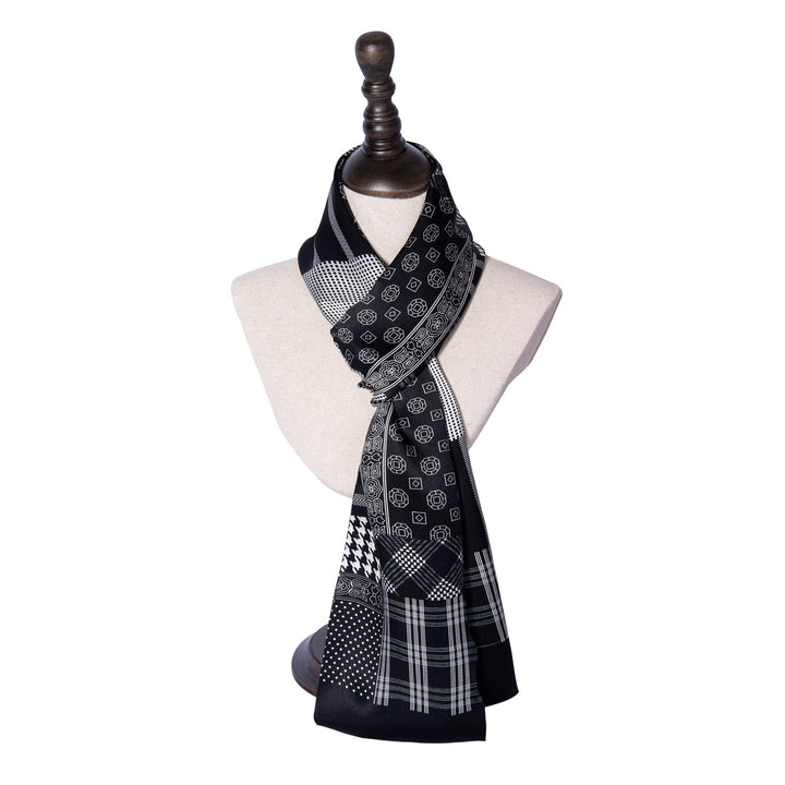 A Mix Pattern Long Silk Scarf by SusanSilk, made of black and white silk and showcasing a blend of geometric shapes, dots, and checks, is elegantly draped around a mannequin bust on a stand.