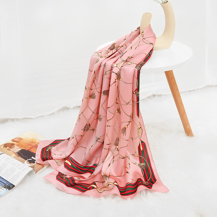 An Ornament & Floral Long Silk Crepe Scarf by SusanSilk, featuring a chain and feather pattern in pink, was draped over a white table with wooden legs on a white fluffy rug next to an open magazine.