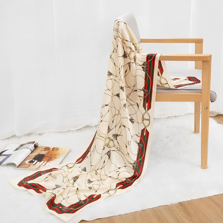An Ornament & Floral Long Silk Crepe Scarf by SusanSilk with a red and green border is draped over a wooden chair, next to an open magazine on a white shag rug.