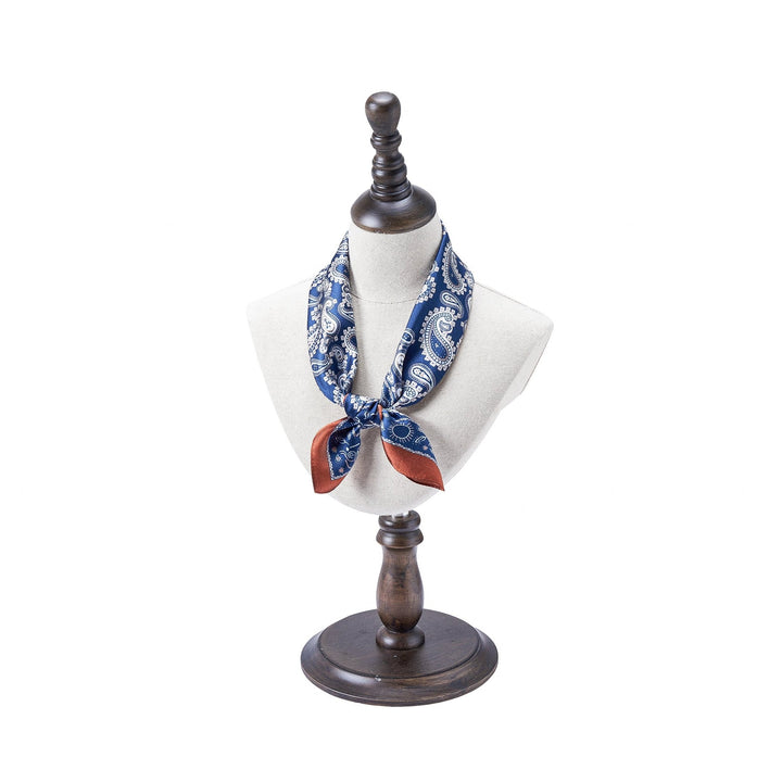 Mannequin with a dark wooden stand displaying a SusanSilk Paisley Series Square Silk Scarf in blue and white, tied with copper-brown ends.