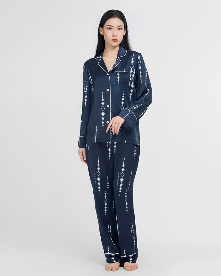A woman stands in a full-length shot wearing the Diamond Striped Silk Pajamas Set, a navy blue ensemble with white geometric patterns from SusanSilk.