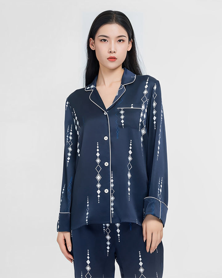 A woman stands wearing the Diamond Striped Silk Pajamas Set by SusanSilk, featuring a navy blue silk fabric with a white geometric pattern and a button-up top.