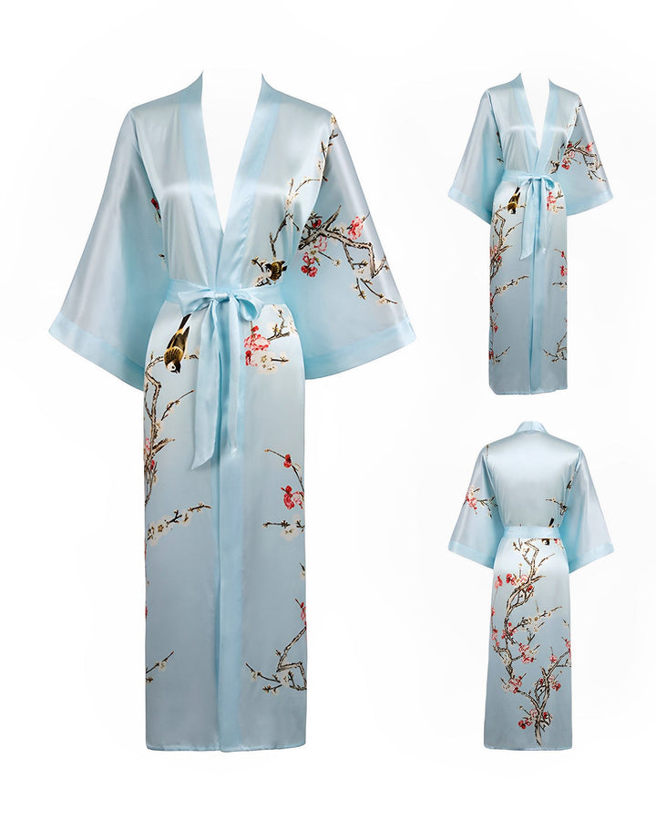 A light blue Plum Blossom Long Silk Kimono by SusanSilk, featuring a cherry blossom and bird design. The kimono has wide sleeves, a tie around the waist, and is shown from front, side, and back views.