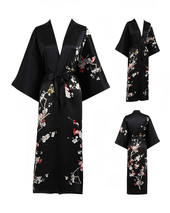 The Plum Blossom Long Silk Kimono by SusanSilk is a black robe adorned with floral and branch patterns. It features wide sleeves, an adjustable waist tie, and is presented from three different angles: front, side, and back.