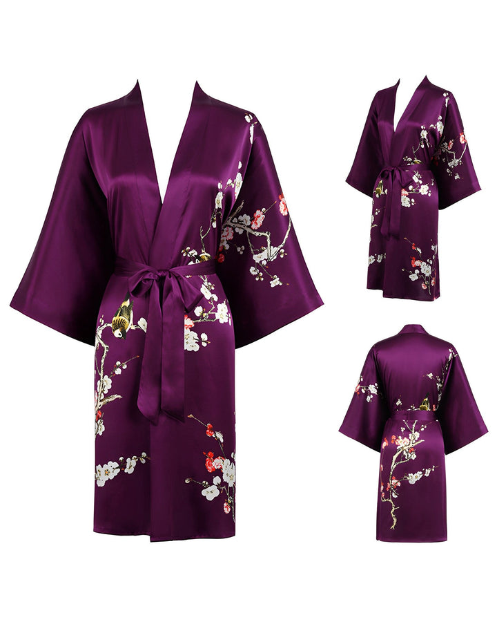 The Plum Blossom Short Silk Kimono from SusanSilk, a stunning purple silky robe adorned with delicate floral patterns, is showcased from multiple angles. The kimono features loose sleeves and a graceful waist tie for an elegant fit.
