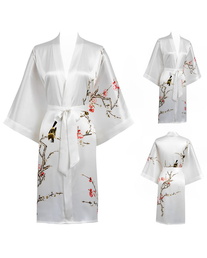 The Plum Blossom Short Silk Kimono by SusanSilk features a bird and cherry blossom branch print, displayed from front and back angles. This white kimono comes with wide sleeves and a tie belt at the waist.