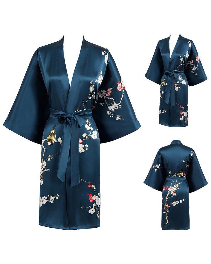 The Plum Blossom Short Silk Kimono by SusanSilk in dark blue features beautiful floral patterns and is shown from front, side, and back views. This elegant kimono has wide sleeves and a tie belt at the waist.