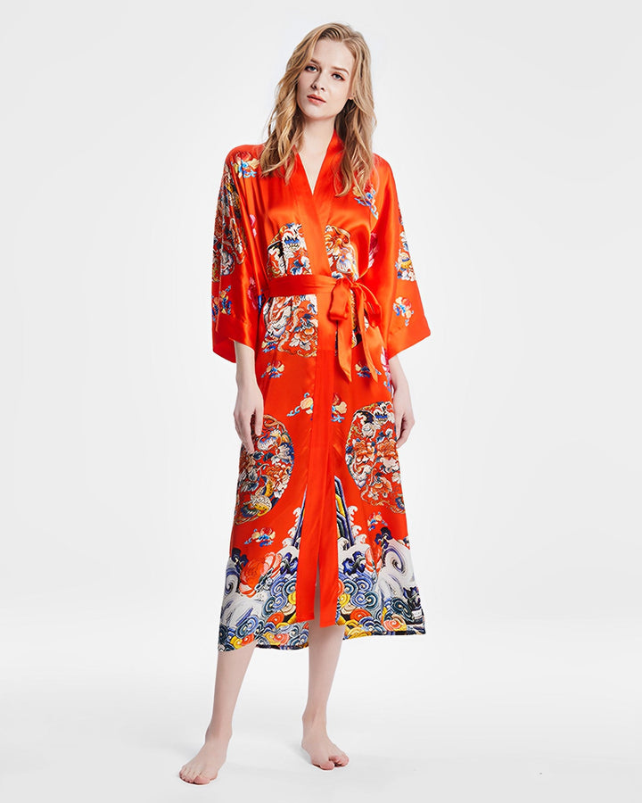 A person stands barefoot wearing a luxurious SusanSilk Wheel of Fortune Long Silk Kimono, featuring a red, patterned design with delicate floral motifs and a cinched waist, posed against a plain white background.#color_orange