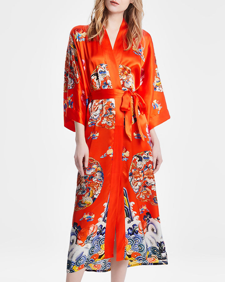 Woman wearing the Wheel of Fortune Long Silk Kimono by SusanSilk, a vibrant red robe adorned with colorful floral and wave patterns, tied at the waist with a matching belt.#color_orange