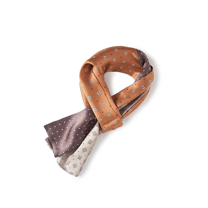 A Tri-Colored Gemstone Narrow Long Silk Scarf from SusanSilk is folded and knotted. It features sections in light brown, off-white, and dark brown with small patterned prints.