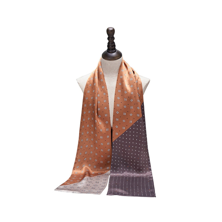 A SusanSilk mannequin displays a Tri-Colored Gemstone Narrow Long Silk Scarf, featuring an orange and brown pattern with small square designs.