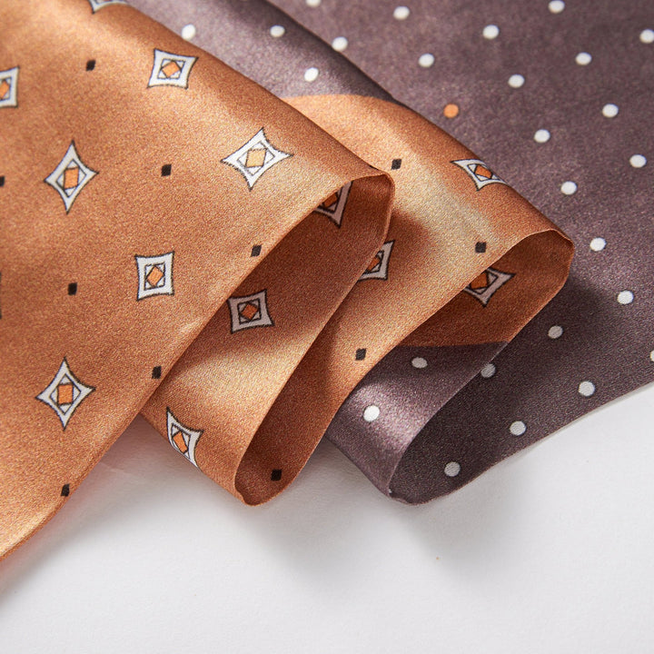 Two Tri-Colored Gemstone Narrow Long Silk Scarves from SusanSilk, one in orange with diamond-shaped patterns and the other in dark brown with white polka dots, are neatly laid on a flat surface.